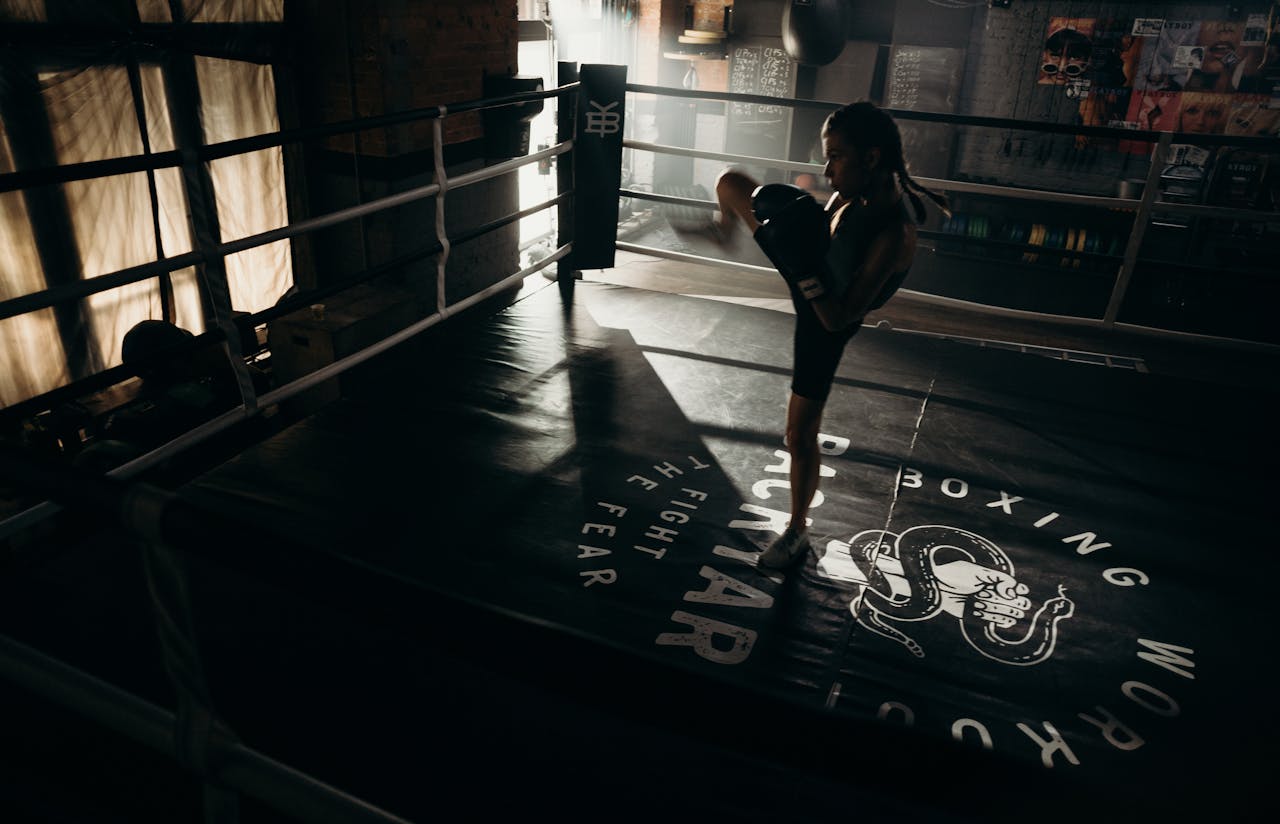 Woman practicing kickboxing in a dimly lit gym, showcasing strength and agility.